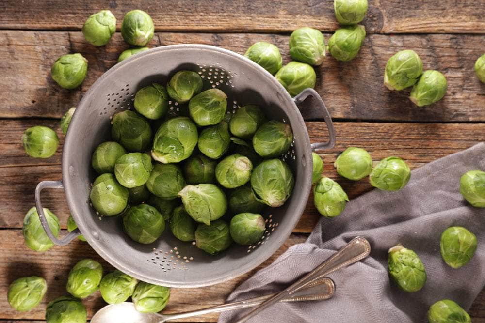 Brussels sprouts displayed in a colander on a wooden table with fabric napkin and cutlery